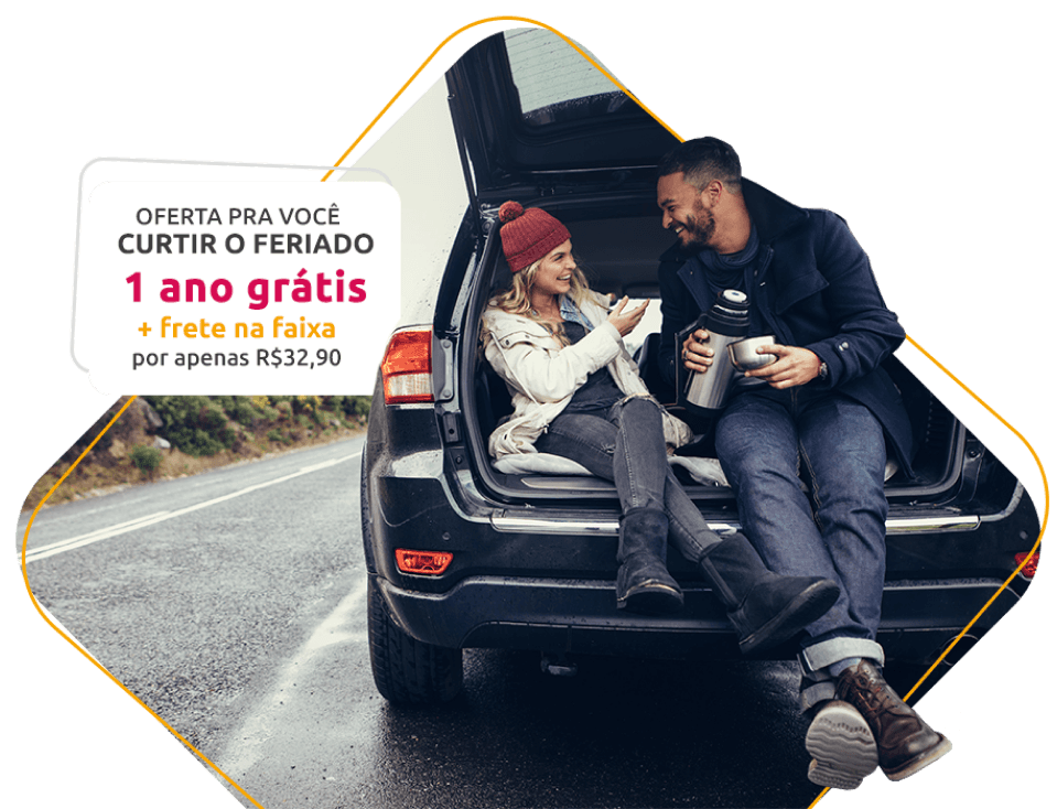 Desktop - Banner promocional - 1 Ano Grátis - Duas pessoas sorrindo e tomando café dentro de um porta malas aberto com o carro parado na estrada.