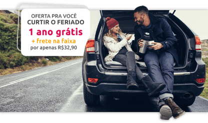 Mobile - Banner promocional - 1 Ano Grátis - Duas pessoas sorrindo e tomando café dentro de um porta malas aberto com o carro parado na estrada.