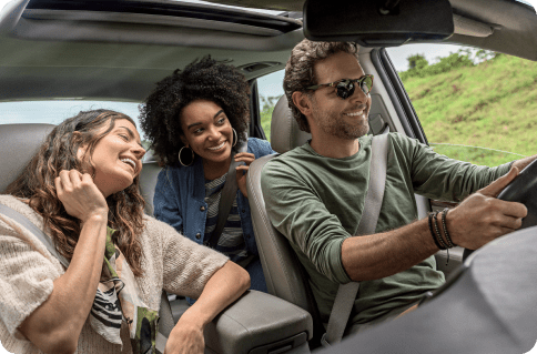 Um homem e duas mulheres dentro do carro, sorrindo enquanto viajam.